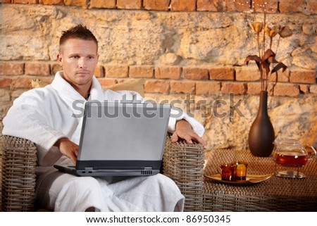 Wellness with laptop computer, young man in bathrobe looking at screen, sitting in armchair.?