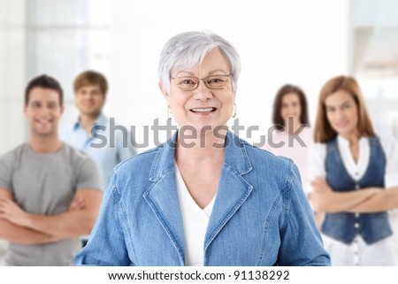 Happy senior teacher looking at camera smiling students in background.?