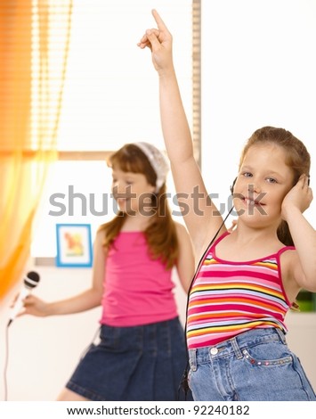 Schoolgirls having fun with headset and microphone, dancing at home.?