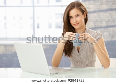 Portrait of smiling woman with laptop computer, holding coffee mug, looking at camera happily.?