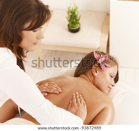 Masseur pressing hands on young woman's back.?