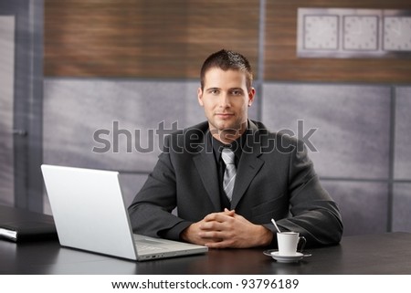 Goodlooking confident manager sitting in fancy office, smiling.?