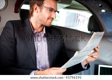 Elegant young man reading newspaper in luxury car.?