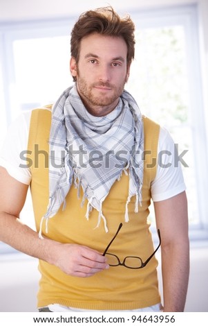 Goodlooking young man standing front of window at home, wearing vest and scarf.?