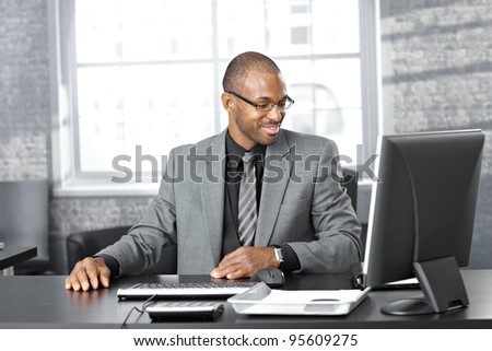 Portrait of happy smart black businessman sitting at desk in office, smiling.?