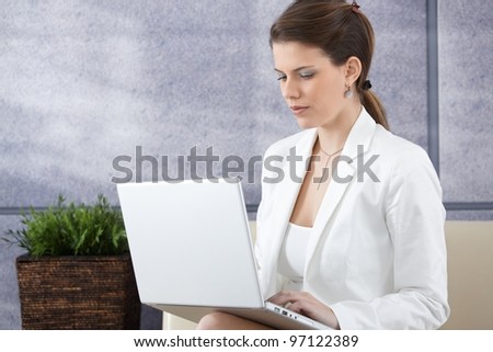 Smart young businesswoman sitting on sofa, working on laptop computer, looking at screen.?