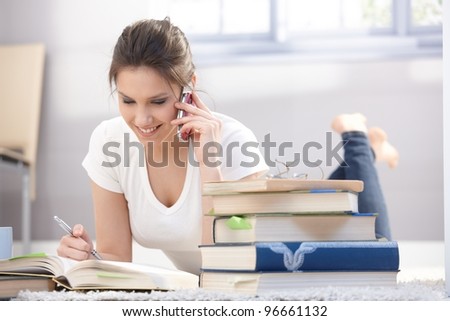 Pretty schoolgirl laying on floor, studying, chatting on mobile phone, smiling.?