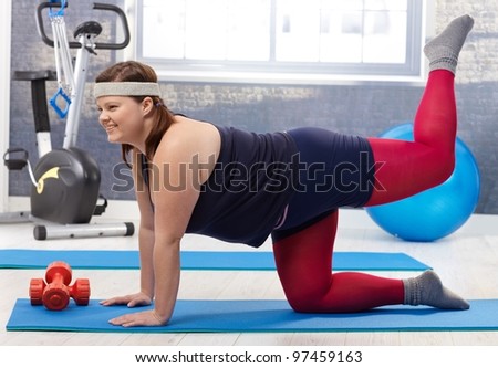 Young fat woman doing gymnastics at the gym, smiling.