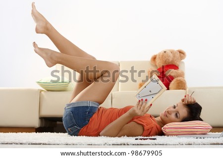 Happy young girl laying on floor at home, looking at boyfriend photo, smiling.