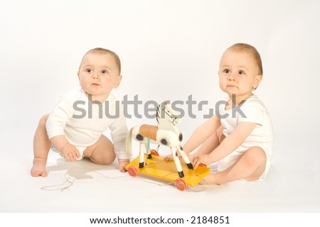 Two toddling boys in white bodysuits with wooden horse