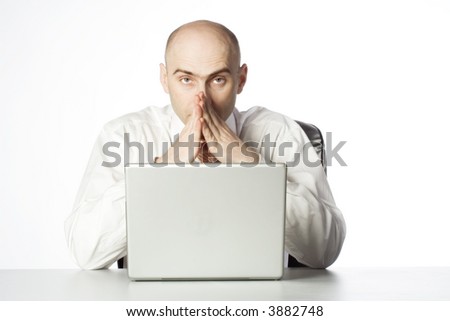 Businessman sits behind laptop with hands tented in front of face in a prayer like pose.