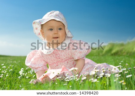 Beautiful baby girl wearing bonnet sat in field of flowers under blue sky.