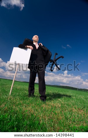 A business executive standing in the countryside with his chair and a signpost. A conceptual picture depicting that he is looking for some office space. Available space for text.