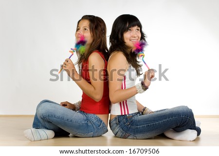 Two teenage girls sitting cross legged holding decorated pencils.