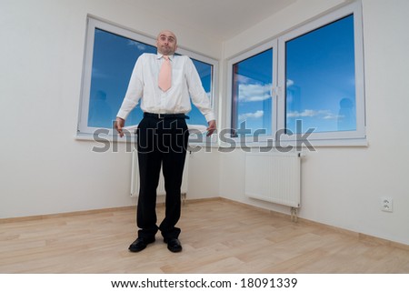 A broke business executive standing in the room of a new house showing his empty pockets.