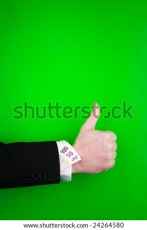 Close up of arm of businessperson giving thumbs up sign with bank notes tucked into suit sleeve, green background.