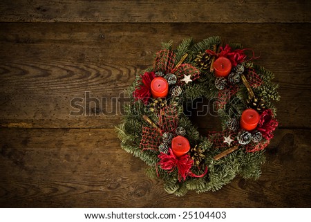 Green christmas wreath decorated with red candles and ribbons, white and golden pine cone, stars and cinnamon on timber floor