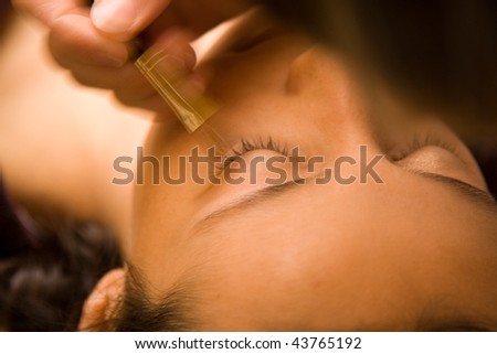 Closeup portrait of reclining young woman seen from top of head using makeup brush.