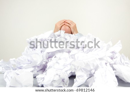 Stressed out man buried in papers holding his head in his hands.