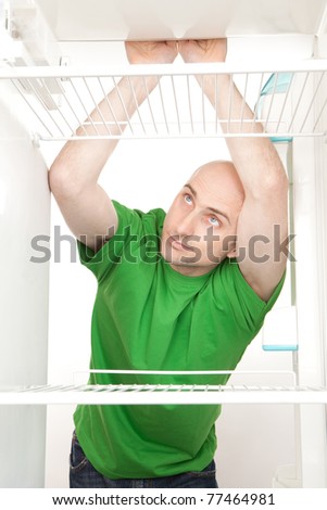 A hungry man leans on a shelf looking for food in an empty fridge.