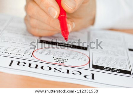 Hand with Red pen Finding a Personal Ad in the Newspaper