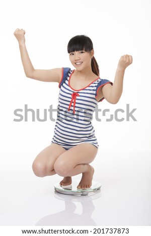 Beautiful Chinese woman weighing herself on a scale and excited with the results isolated on a white background