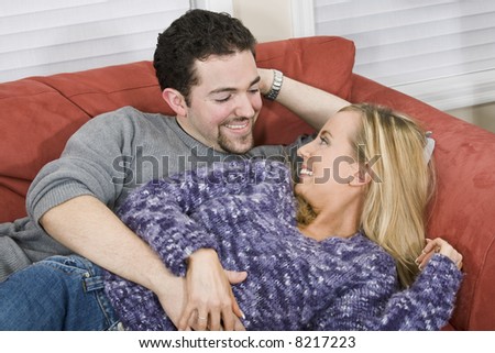 Studio photograph of young Caucasian couple posing with their arms around each other on a white background