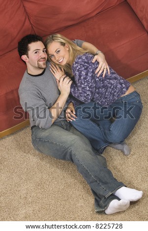 Young Caucasian couple sitting with their arms around each other on the floor