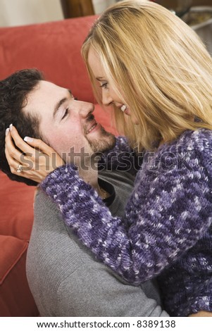 Young Caucasian couple in their early 20s with their arms around each other on a red couch