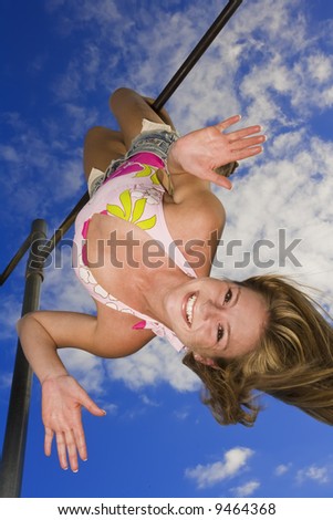 Beautiful Caucasian female teenage hanging upside down on outdoor gym bar and wearing a swimsuit.