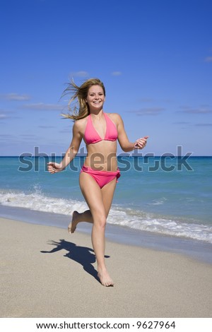 Beautiful Caucasian female teenage running through to surf wearing a colorful bikini.