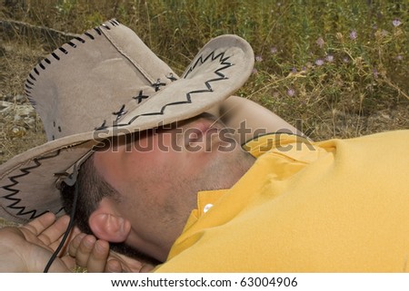Man with cowboy hat  laying in  a grass field. Man resting in the grass