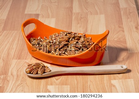 Pecans in an orange bowl with a wood spoon