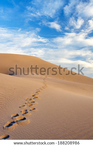 Desert sand dune with foot prints leading to the sky