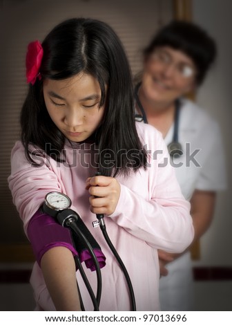 This young girl tries to take her own blood pressure as nurse watches