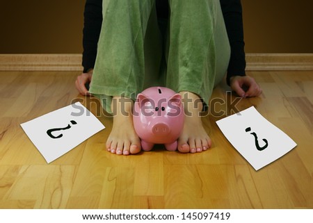 Upset woman sitting on an empty floor, holding a piggy bank and a paper with questions