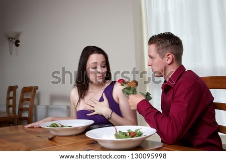 A man handing a red rose to his girlfriend in a restaurant
