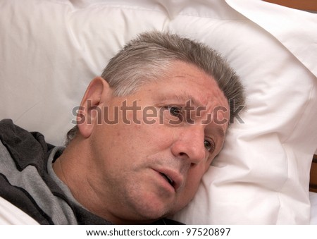 A mature man looking distressed while laying in bed