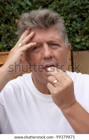 A mature man taking medication for a headache