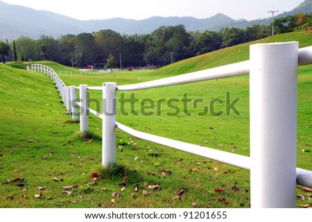 A photo of white fence on green hill side.