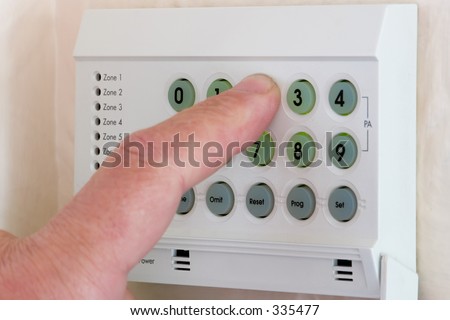 A finger entering a code into the keypad of a home burglar alarm