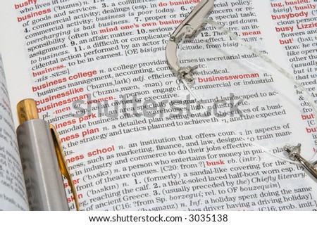 A dictionary opened at different business definitions with a pen and glasses on it