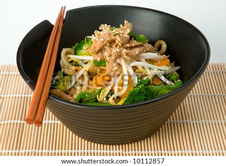 Asian stir fry with Shanghai noodles, pork, vegetables, bean sprouts and sesame seeds, with chopsticks on bamboo mat