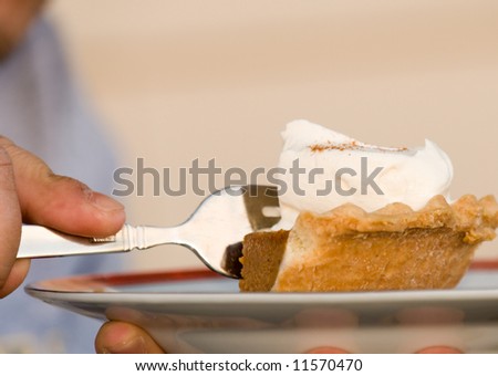 Man holding a plate and eating a piece of pumpkin pie with whipped cream