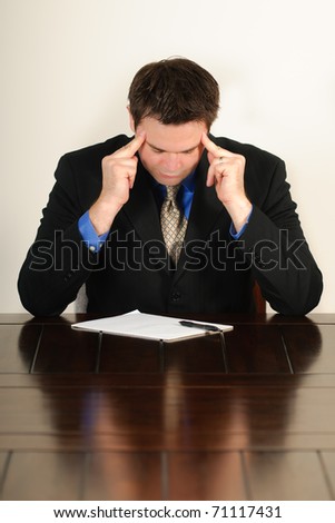 Single man in  business attire sitting at a table working and feeling frustrated