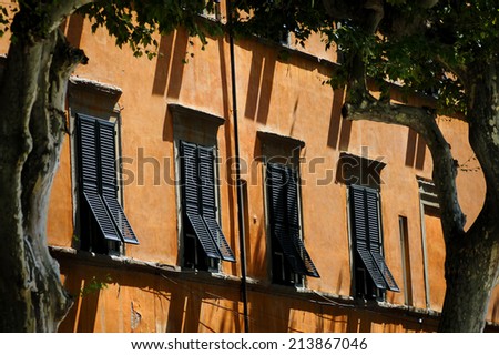 Jalousie windows in a row, over beautiful, pastel orange facade, through frame of two trees and shadows