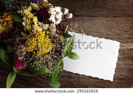 Bouquet of dried flowers and empty paper card on a wooden background.