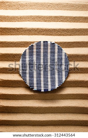 Round striped cloth on a striped sandy background.