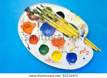 Set of brushes and a palette of colorful paint samples on a blue background.