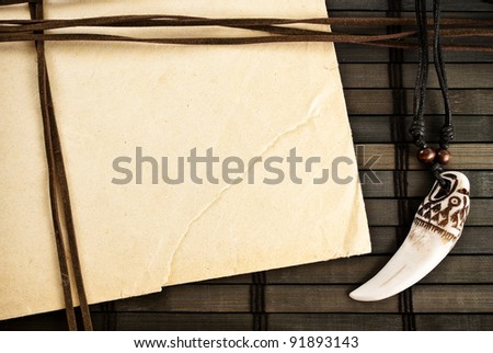 Background of paper sheet, decorative trophy tooth and leather straps on a wooden background.